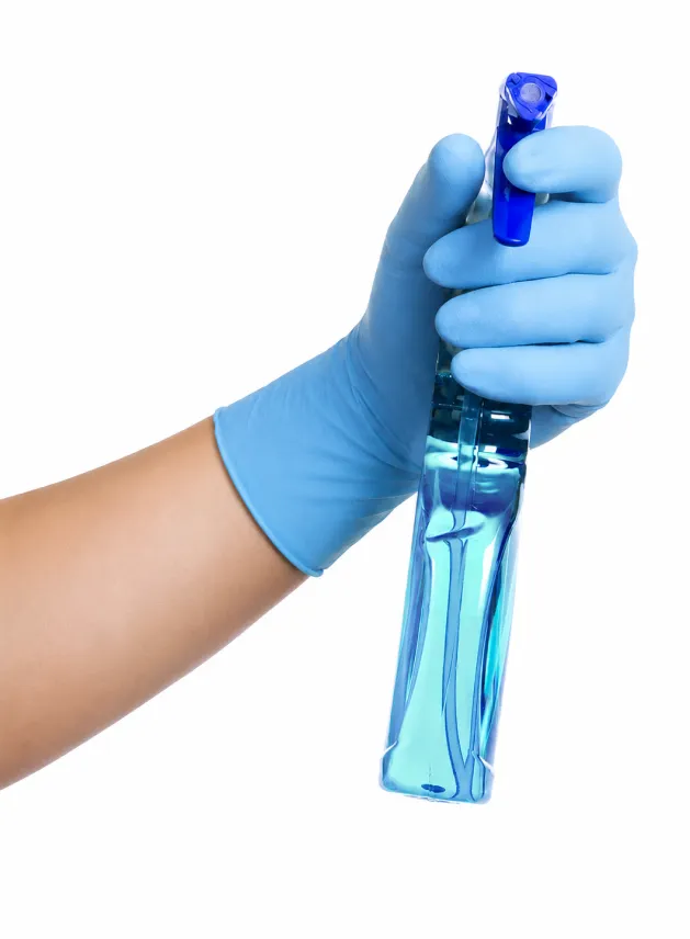 Mano con guanto protettivo che impugna un detergente spray professionale